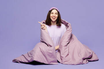 Full body young calm woman wear pyjamas jam sleep eye mask rest relax at home sit wrapped in blanket point finger aside isolated on plain pastel purple background studio. Good mood night nap concept.