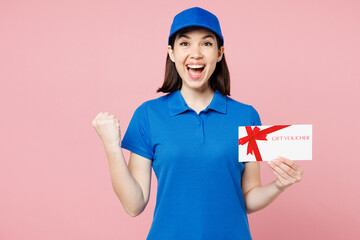 Delivery girl employee woman wears blue cap t-shirt uniform workwear work as dealer courier hold gift coupon voucher card do winner gesture isolated on plain pastel pink background. Service concept.