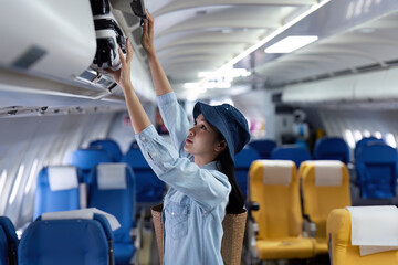 female passenger keep bag in the compartment above the seat in the plane. travel concept