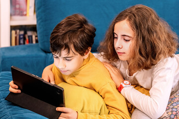 Two Kids Sharing a Tablet on a Cozy Sofa