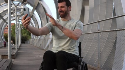 Happy middle-aged man in a wheelchair engages in a video call, showcasing modern accessible urban spaces. Cheerful Man in Wheelchair Having a Video Call on Urban Bridge