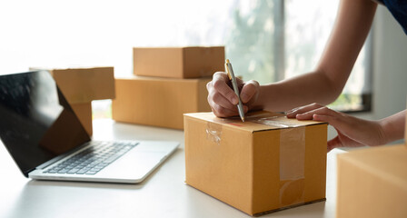 A small business owner receives product orders and writes shipping information on cardboard boxes...