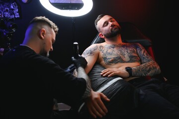 Portrait of a tattoo master showing a process of creation tattoo on a hand under the lamp light