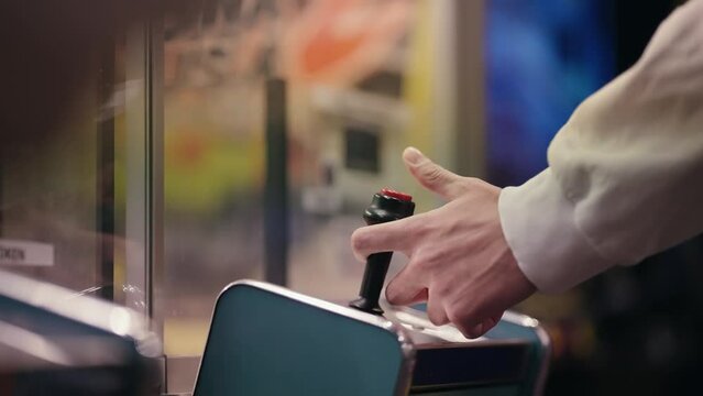 A person is playing a crane game at a carnival moving the joystick. The game is a claw machine, and the person is trying to grab a stuffed animal