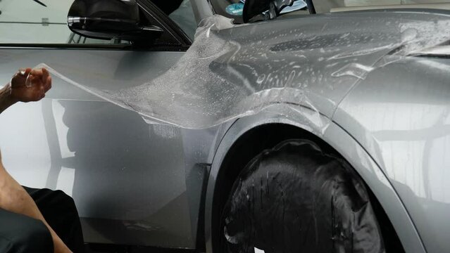 Close up of paint protection film installation on front bumper of modern luxury car. PPF is polyurethane film applied to car surface to protect the paint from stone chips, bug splatter, and abrasion.