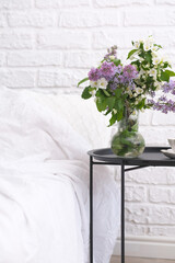Spring morning in cosy bedroom: coffee table with bouquet of different flowers, cup of coffee,...