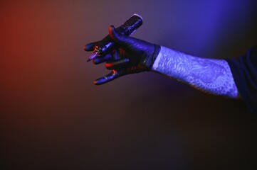 Closeup of tattooer master's hand in black glove holding machine for making tattoo art on body isolated on dark background in neon.