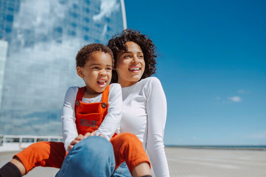 Young multiethnic mother and daughter happy smiling, enjoying together outdoors during a bright day. Spring, summer vacations, lifestyle, maternity concept.