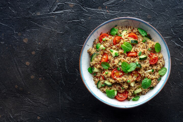 Quinoa tabbouleh salad in a bowl, a healthy dinner with tomatoes and mint, shot from above with a...