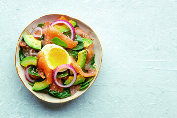 Salmon, avocado and egg salad with fresh leaves and onions, overhead flat lay shot on a slate background. Healthy diet, with a place for text