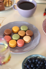 Plate of pastel macarons, cookies and chocolate, cup of tea of coffee, glass of bubble water, various berries, books and accessories on the table. Selective focus, pastel colors.