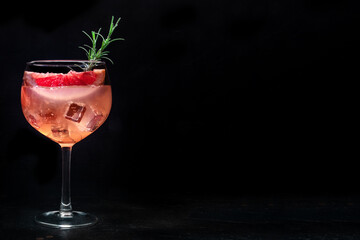 Fancy cocktail with fresh fruit. Gin and tonic drink with ice at a party, on a black background. Alcohol with pink grapefruit and rosemary, with copy space