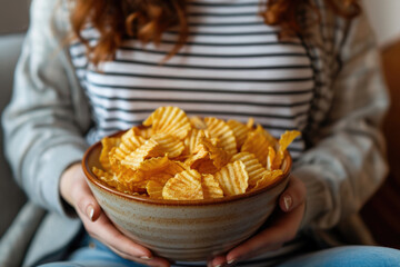 Pregnant woman sitting on the sofa enjoys eating potato chips from a bowl at home. ai generated