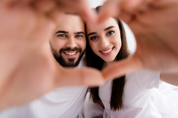 Photo of pretty adorable couple wear white t-shirts embracing showing arms heart indoors apartment bedroom