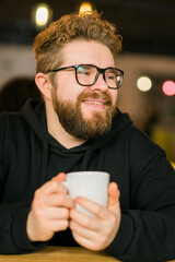 Bearded curly man smiling confident drinking coffee in restaurant or coffee shop. Millennial...