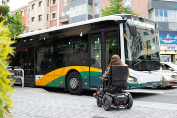 woman in an electric wheelchair waits for an accessible city bus. urban mobility for people with motor disabilities.