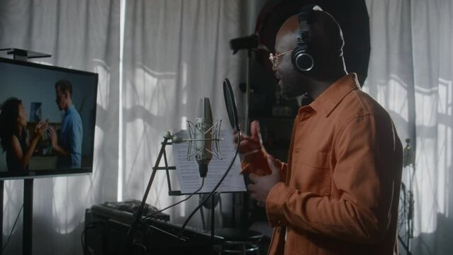 Medium shot of African American male voice-over actor in headphones performing part for dubbing of foreign TV movie in recording studio, of multiethnic couple fighting, woman slapping man on face