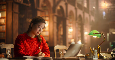 Asian Female Student Engaged in Studying With Books and Laptop in Classical Library Setting. Young...