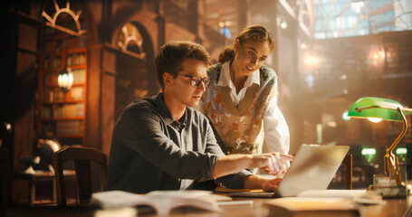 Female and Male Students Studying in a College Library. Female Helping Her Classmate Colleague with Homework on a Laptop Computer. Couple Using Laptop Computer for a Group Research Project