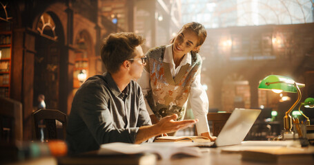 Engaged Caucasian Female Student Discussing Academic Material with Male Peer in a Historic Library. Both Using Books and Laptop for Research, Surrounded by Wooden Shelves and Classical Architecture.