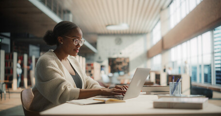 Dedicated African American Female Student Engaged in Online Learning at a Modern Library. Young...