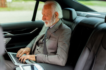 Elder gentleman typing intently on laptop in the comfort of his car
