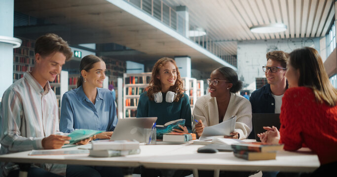 Diverse Group of Students Collaborating on a Project in a Modern Library. Young Men and Women Using Laptops and Books, Engaging in Group Discussion and Learning Together.