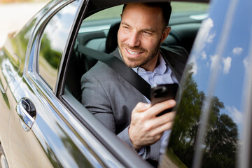 Businessman in a gray suit engaged with smartphone during sunny day car ride