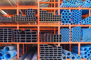 Various sizes of many Carbon Steel rectangular and Square Tubes with blue PVC water Pipes on Storage Shelf of building Supply Store