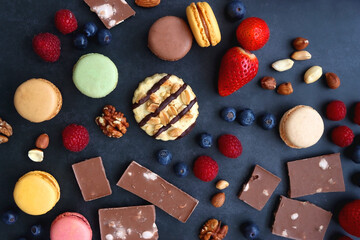 Macarons, chocolate, cookies, berries and various nuts on dark blue background. Top view.