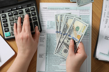 Payroll. Woman with dollar banknotes and calculator planning budget at wooden table, top view