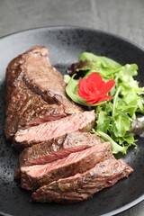 Pieces of delicious grilled beef meat and greens on table, closeup