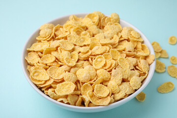 Breakfast cereal. Tasty corn flakes in bowl on light blue table, closeup