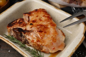 Tasty marinated meat and rosemary in baking dish on wooden table, closeup