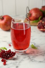 Tasty pomegranate juice in glass and fresh fruits on white marble table