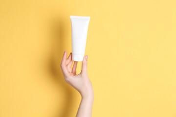 Woman holding tube of cream on yellow background, closeup. Space for text