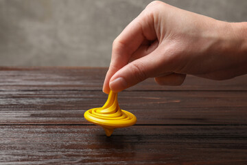 Woman playing with yellow spinning top at wooden table, closeup
