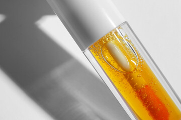 Fototapeta premium Orange lip gloss on white background, closeup. Space for text
