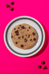 Chocolate chip cookie on a plate against a vivid pink background