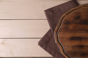 Cutting board and napkin on beige wooden table, top view. Space for text