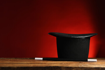 Magician's hat and wand on wooden table against red background, space for text