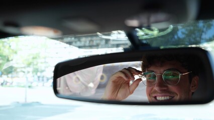 Male driver adjusting his glasses and looking in the rear view mirror while driving in a car in the city. Transport and lifestyle concept. Real time