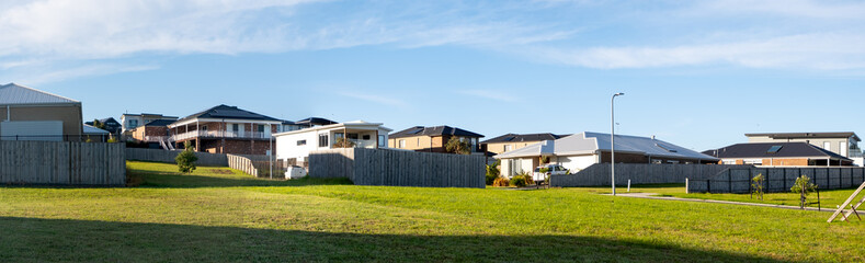 Panoramic view of a large vacant land lot with some residential suburban houses in the background. Panorama of Australian homes in a neighbourhood. Real estate, housing. San Remo VIC Australia