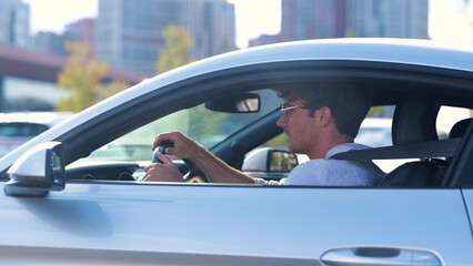 Happy young man in glasses driving his car with open window, looking on the road. Side view. Transport and lifestyle concept. Real time