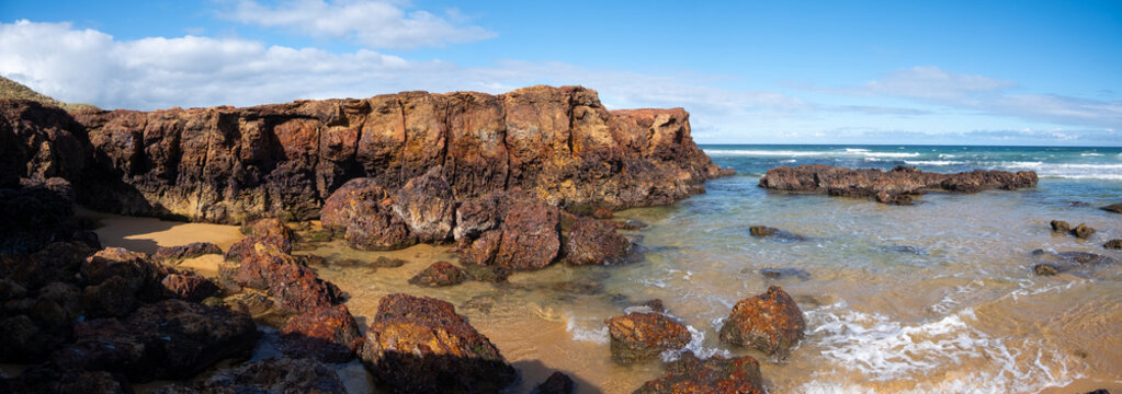 Panoramic coastal scenery rugged beach at Forrest Caves at Bass Strait, formed by rock erosion of cliffs. The eroding, red, basalt bluffs. Phillip Island, VIC Australia.