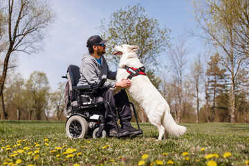 Man with disability outside in park with his service dog using electric wheelchair.