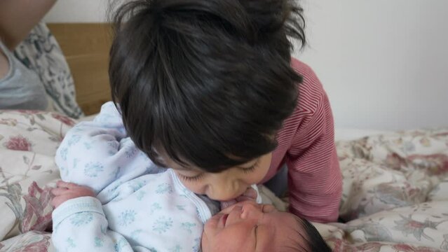 Child kissing newborn baby brother in hand laid in bed in the morning, authentic family lifestyle. real life interaction between infant initial stages of life with sibling