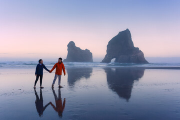 Asian couple enjoying on Wharariki beach with iconic archway island at New Zealand