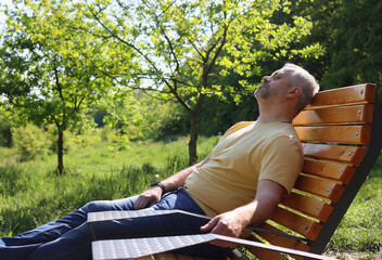 A gray-haired middle-aged man is resting in a summer park. Mental health, meditation, recovery from...