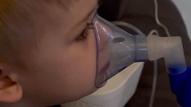 Close up of little sick boy holding a inhalation mask on his face to breath saline solution 
